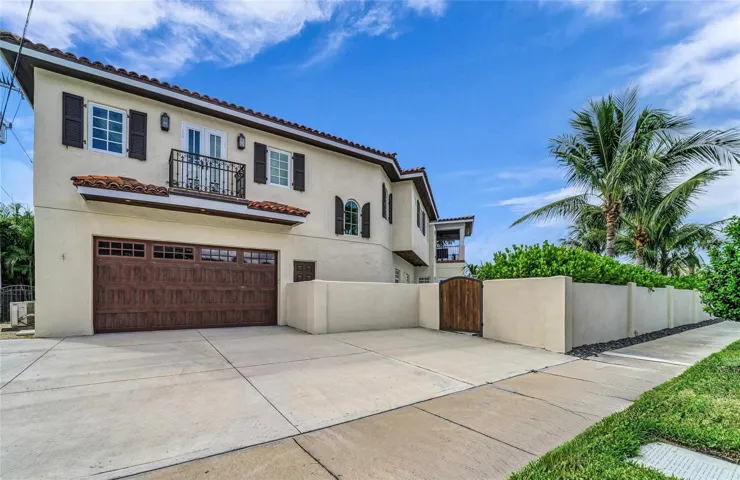 View from the sidewalk of privacy wall, garage, back driveway and Juliet balcony of apartment.