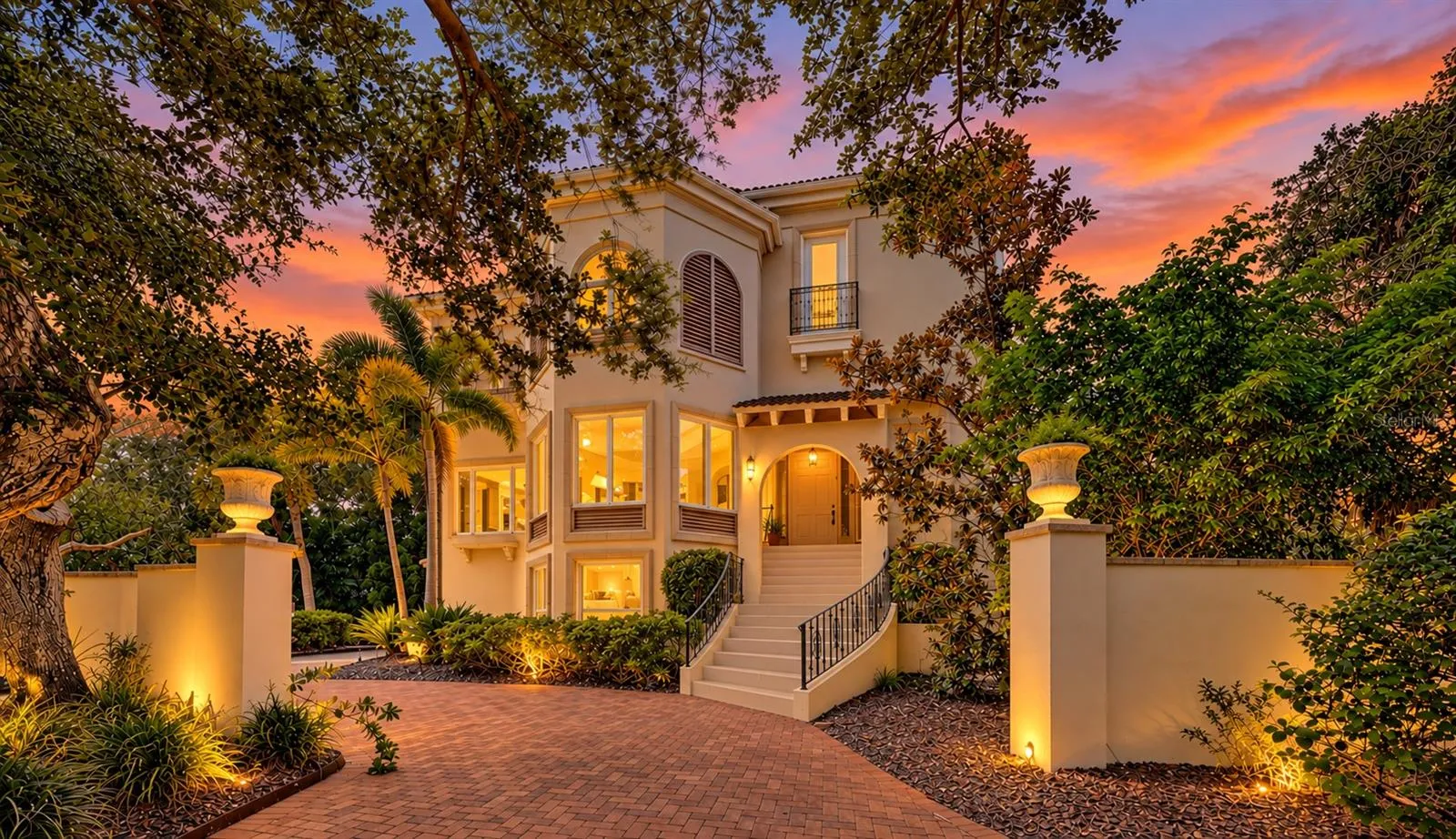 Warm architectural lighting and mature oaks create a striking sense of arrival as evening falls.