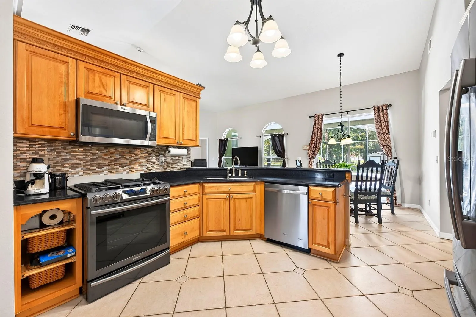 The Kitchen is both spacious and functional, featuring an abundance of SOLID-WOOD CABINETRY, generous counter space, modern tile backsplash, STAINLESS-STEEL APPLIANCES, pantry closet and breakfast bar.