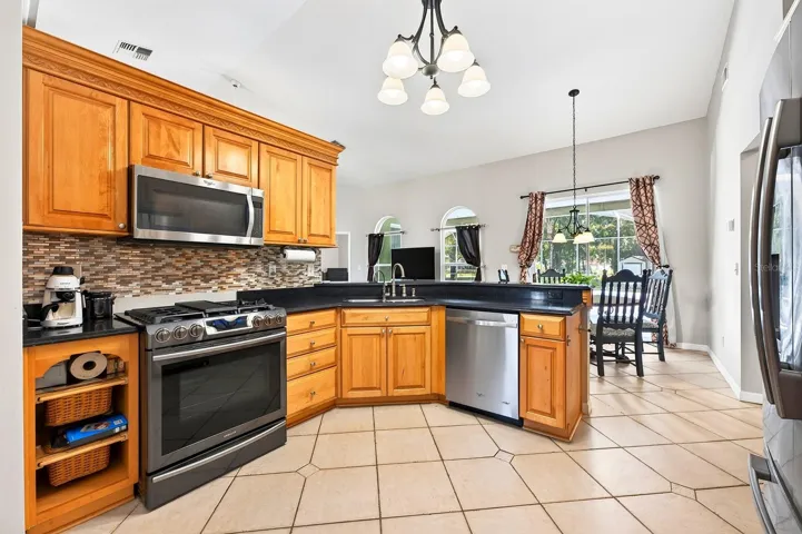 The Kitchen is both spacious and functional, featuring an abundance of SOLID-WOOD CABINETRY, generous counter space, modern tile backsplash, STAINLESS-STEEL APPLIANCES, pantry closet and breakfast bar.