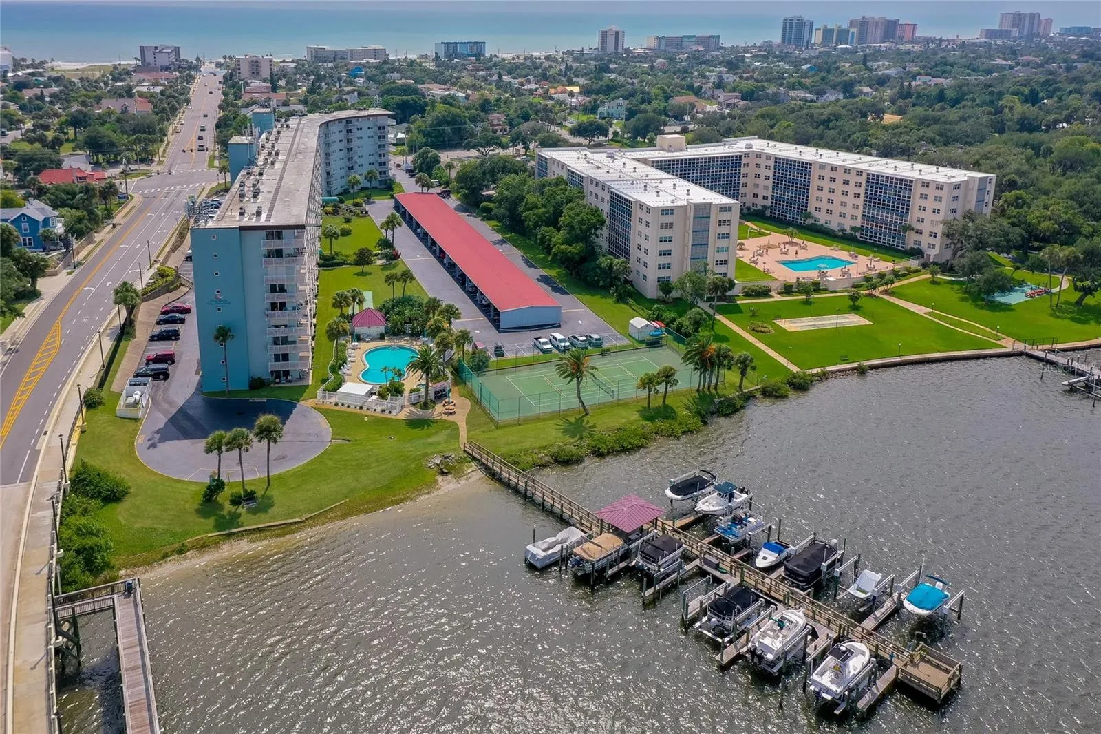 Expansive aerial perspective showcasing the community’s private dock, waterfront setting, pool, and tennis court, all just moments from the beach.