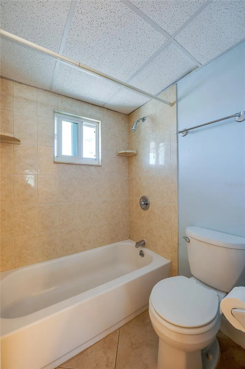 Full bathroom with a tiled tub and shower combination, complete with a window for natural light and ventilation.
