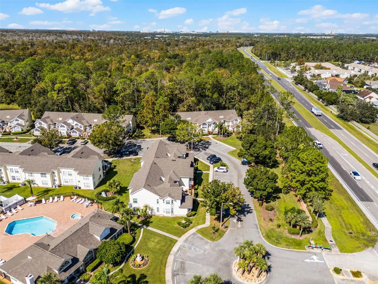 Community Entrance &amp; Highway Proximity: Aerial overview featuring the main community drive, entrance roundabout, amenity center, and adjacent major roadway for easy commuting.