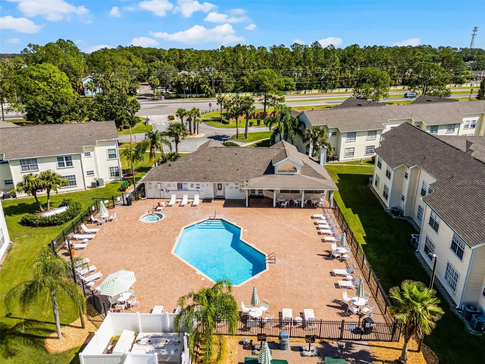 Pool &amp; Spa Complex: Overhead aerial capture of the sparkling resort pool, heated spa, paved lounge deck, covered clubhouse patio, and tropical landscaping.