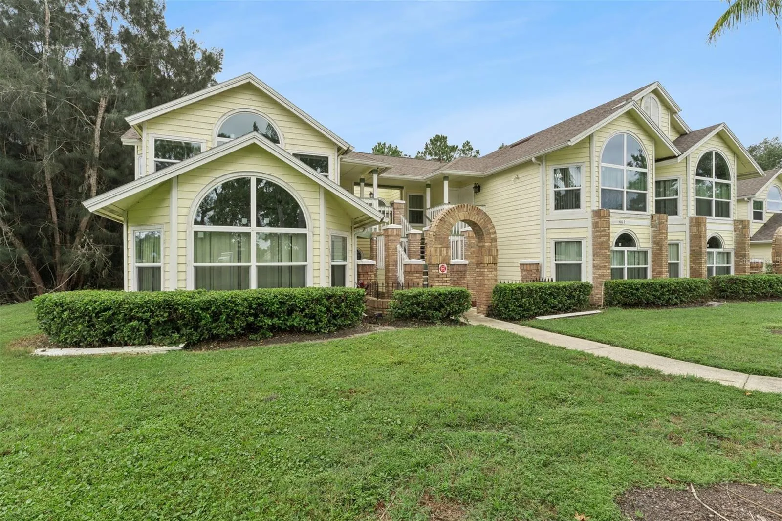 Exterior Side View: Angled building view highlighting grand arched windows, brick accents, low-maintenance hedge landscaping, and lush lawn.