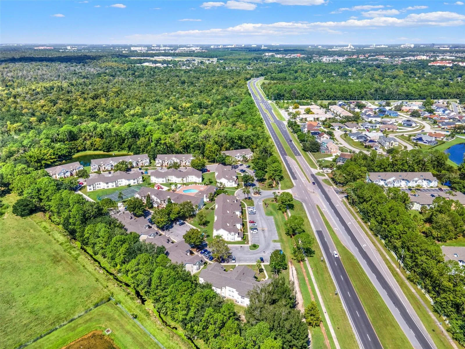Regional Overview Aerial: High-altitude aerial view showcasing the entire community grounds, surrounding lush foliage, adjacent pond, and convenient highway access.