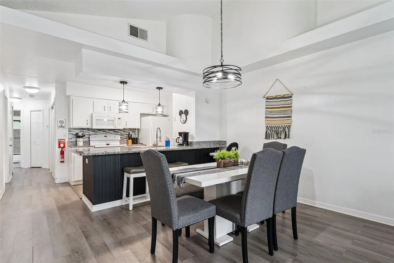 Dining &amp; Kitchen Flow: View of the dining area looking into the open kitchen, featuring high ceilings, modern pendant lighting, wood-look plank flooring, and a sleek breakfast bar.