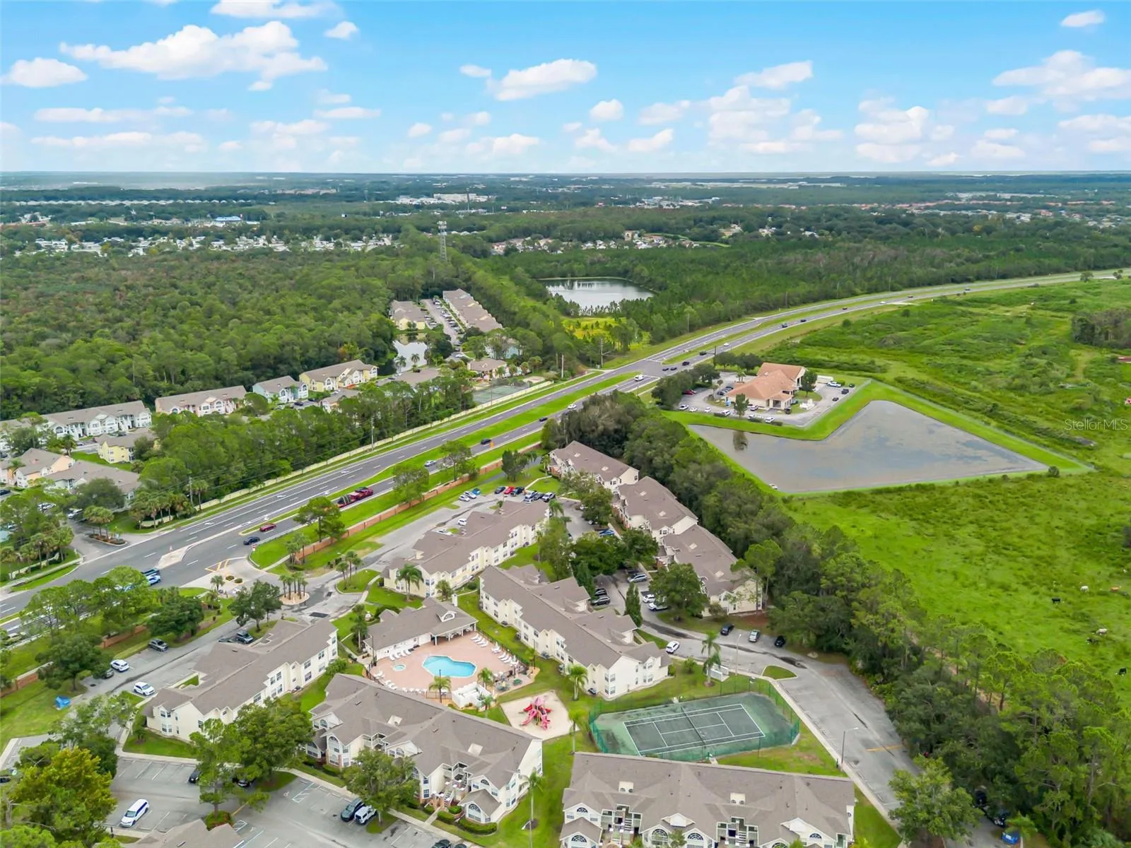 Community &amp; Highway Aerial: High-angle drone shot capturing the full neighborhood grounds, recreational amenities, retention ponds, and direct access to nearby thoroughfares.
