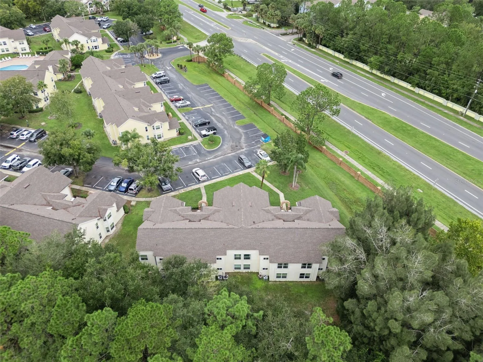 Aerial View of Rear &amp; Grounds: Elevated aerial angle looking over mature tree tops toward the building rear, parking facilities, and nearby main road