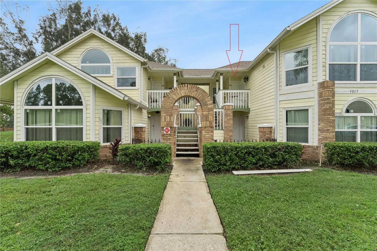 Building Elevation: Multi-unit building exterior featuring pastel siding, decorative brick archway entry stairs, large architectural windows, and manicured landscaping.