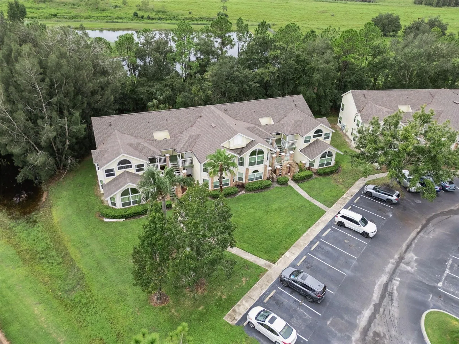 Aerial Setting &amp; Conservation View: High-angle aerial view showcasing the building tucked alongside a peaceful water feature and lush wooded backdrop