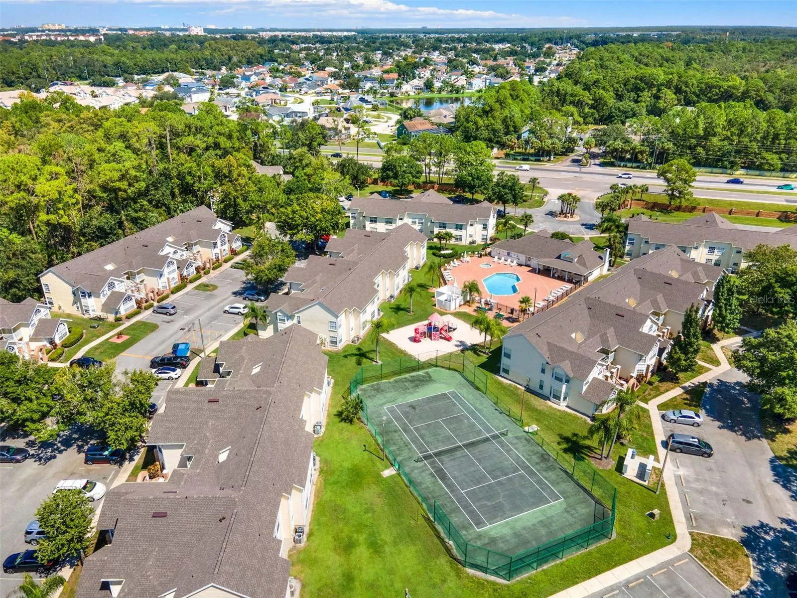 Recreational Facilities Aerial: Elevated aerial view highlighting the outdoor tennis court, resort pool complex, playground area, and manicured green spaces.