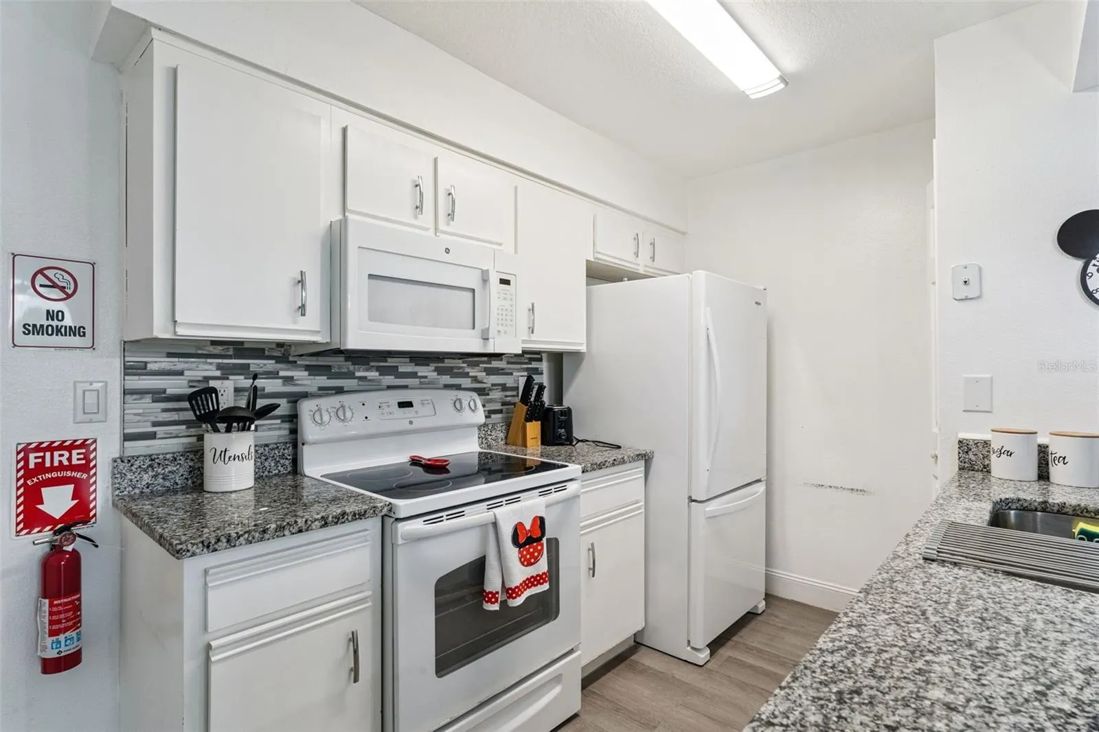 Kitchen Interior: Bright kitchen equipped with clean white cabinetry, granite countertops, a mosaic tile backsplash, electric range, and matching white appliances.