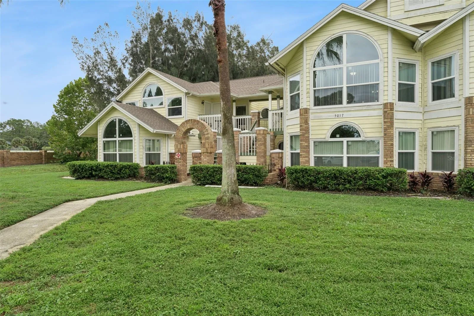 Front Walkway &amp; Entry: Paver walkway leading up to the brick entry archway, framed by mature palm trees and green space.