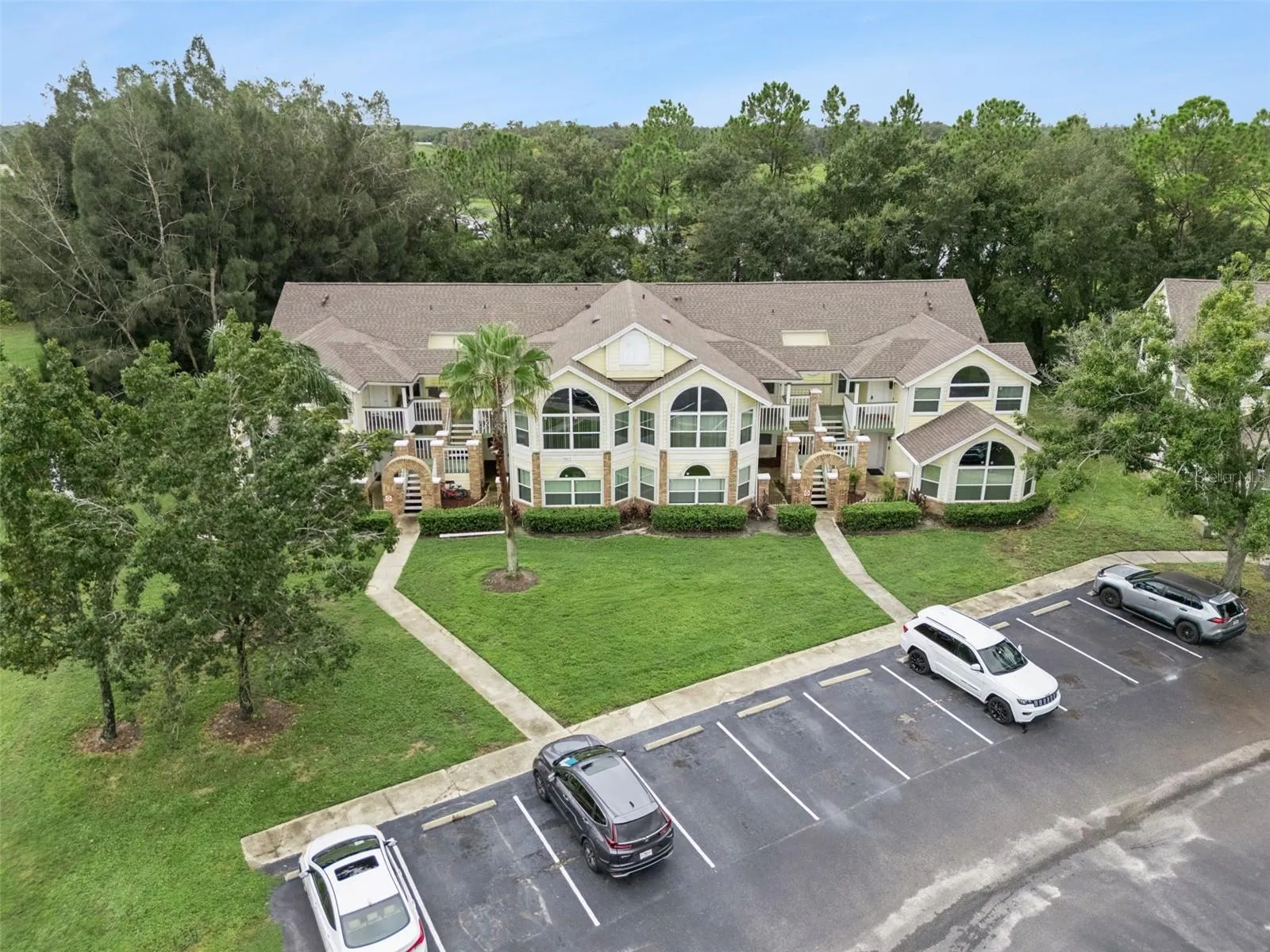 Exterior Aerial Perspective: Front aerial view displaying the building facade, brick architectural entries, central palm landscaping, and parking lot