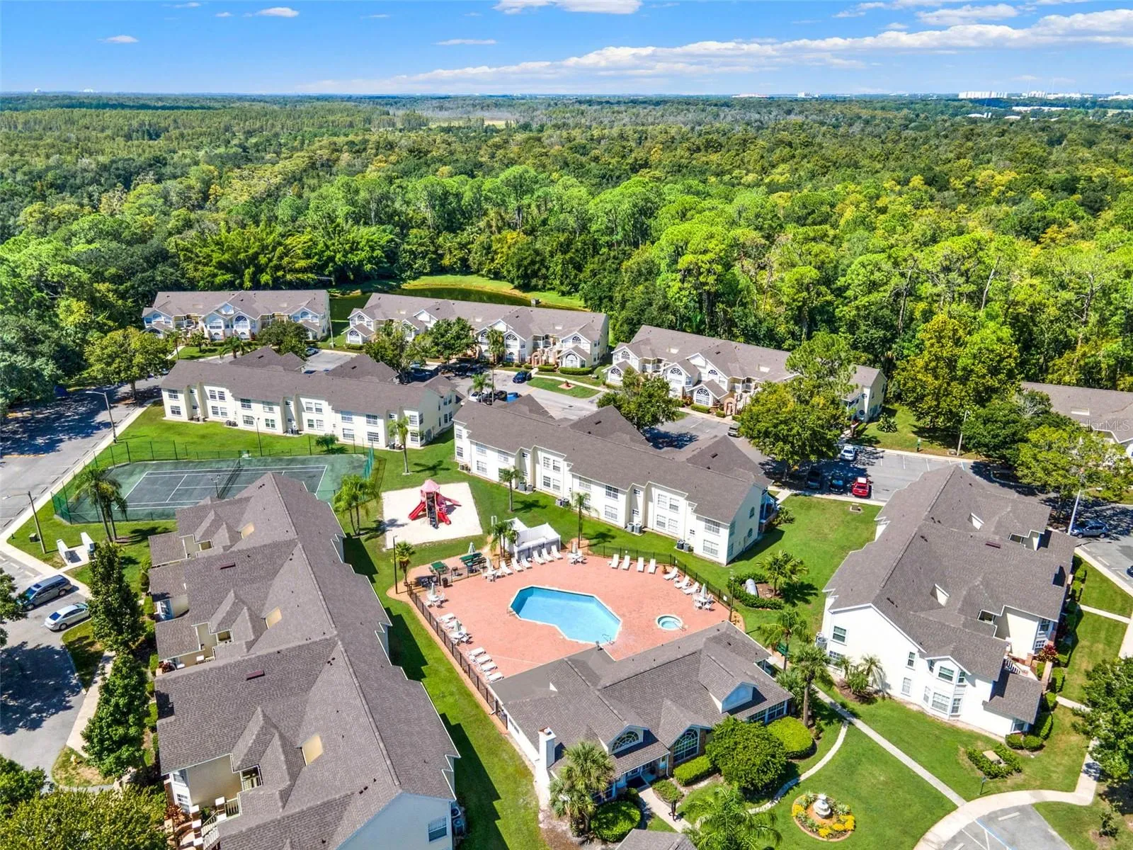 Pool &amp; Amenity Deck Aerial: Close-up aerial view centered on the resort-style swimming pool, heated spa, sunbathing patio, playground, tennis court, and clubhouse.