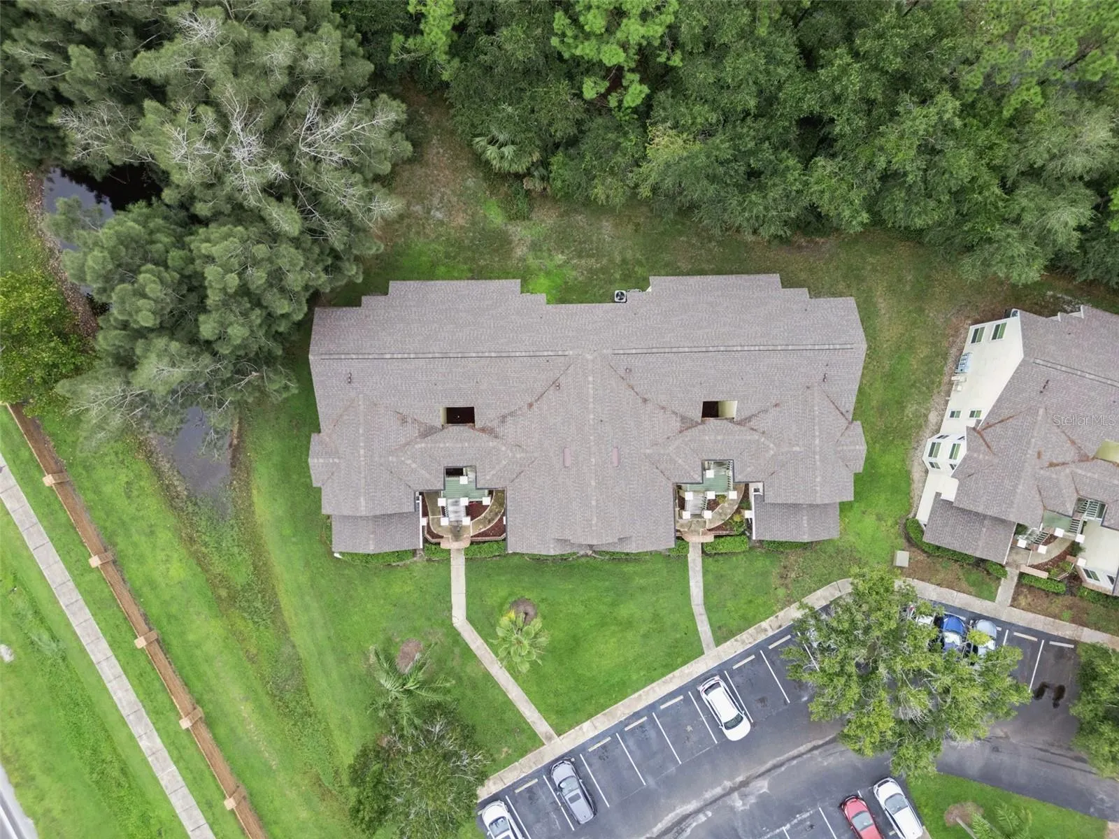 Top-Down Aerial View: Direct overhead drone perspective highlighting the building roofline, front entryway paths, and mature tree borders