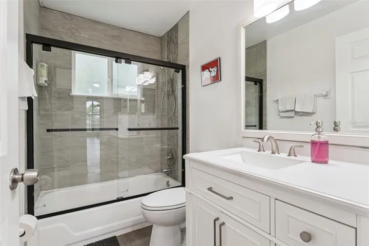 Full Bathroom &amp; Shower: Updated full bathroom complete with a white vanity, modern matte black sliding glass shower doors, and sleek tile surround.