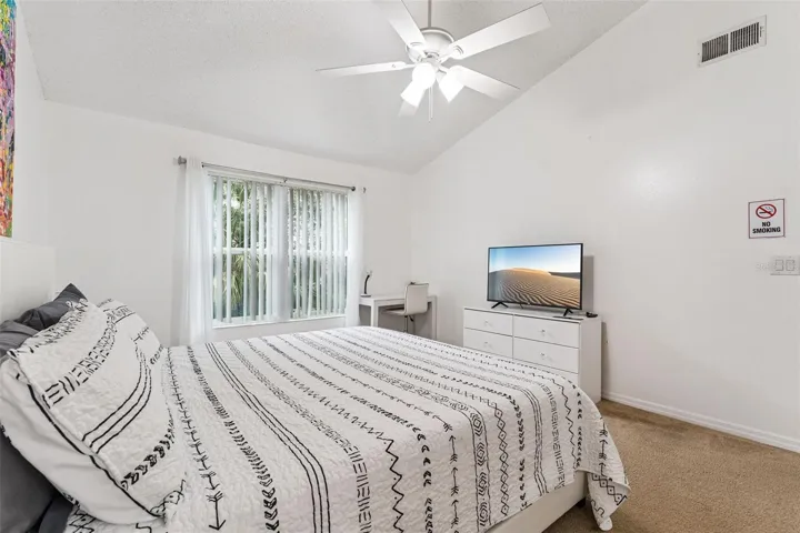 Primary Bedroom: Bright primary bedroom featuring vaulted ceilings, a ceiling fan, plush carpeting, dedicated work/desk nook, and large window for natural light.
