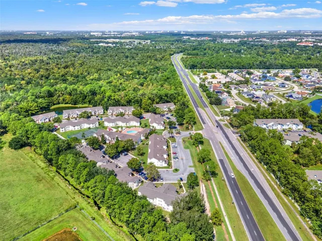 Regional Overview Aerial: High-altitude aerial view showcasing the entire community grounds, surrounding lush foliage, adjacent pond, and convenient highway access.
