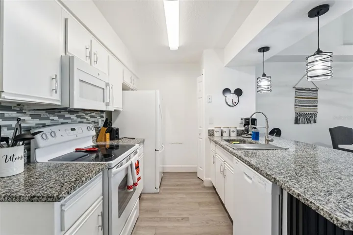 Kitchen &amp; Breakfast Bar: Kitchen perspective highlighting durable granite counters, undermount sink with goose-neck faucet, dishwasher, and modern pendant lights over the peninsula.