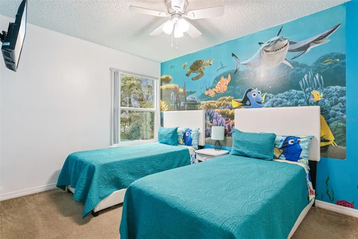 Underwater-Themed Twin Bedroom: Fun themed guest bedroom with dual twin beds, vibrant ocean wall mural, ceiling fan, carpet flooring, and wall-mounted TV.