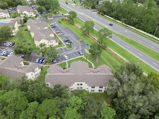 Aerial View of Rear &amp; Grounds: Elevated aerial angle looking over mature tree tops toward the building rear, parking facilities, and nearby main road