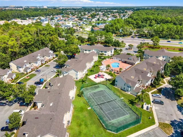 Recreational Facilities Aerial: Elevated aerial view highlighting the outdoor tennis court, resort pool complex, playground area, and manicured green spaces.