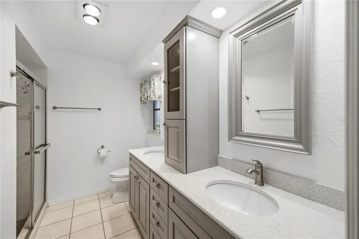 Remodeled primary ensuite bathroom with wood cabinets, quartz counters, dual sinks and shower