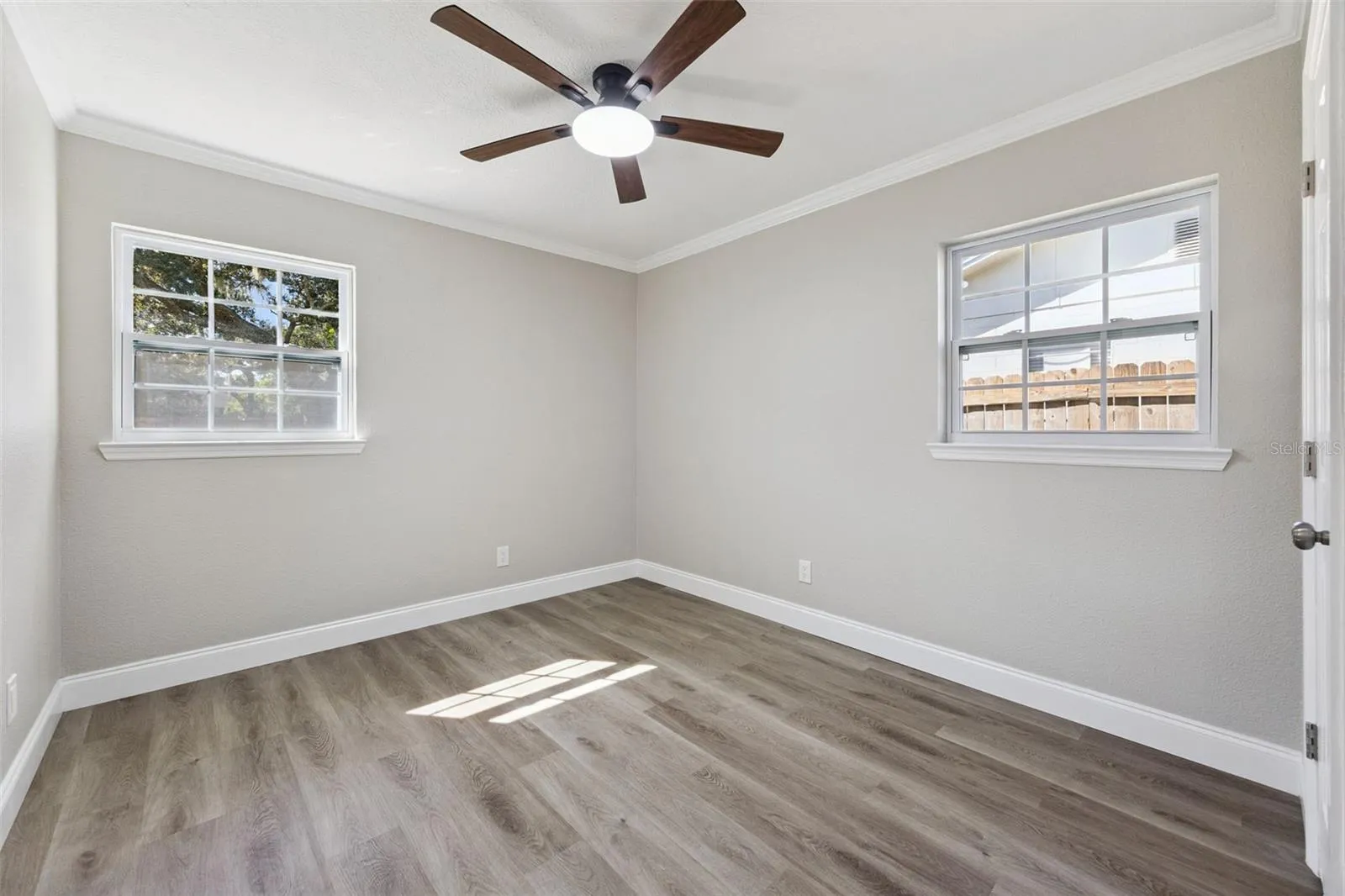 Guest Bedroom: Additional guest bedroom with dual windows offering abundant natural light, modern ceiling fan, crown molding, and wood-look plank flooring.