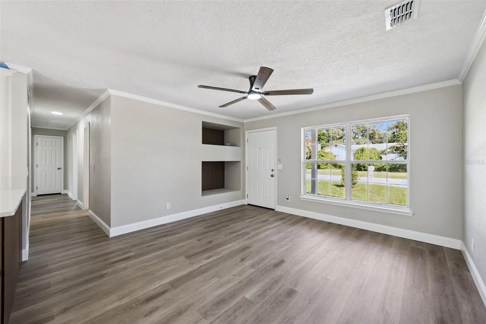 Living Room &amp; Recessed Niches: Spacious main living room highlighting built-in wall display niches, modern ceiling fan, large front window, and durable vinyl plank flooring