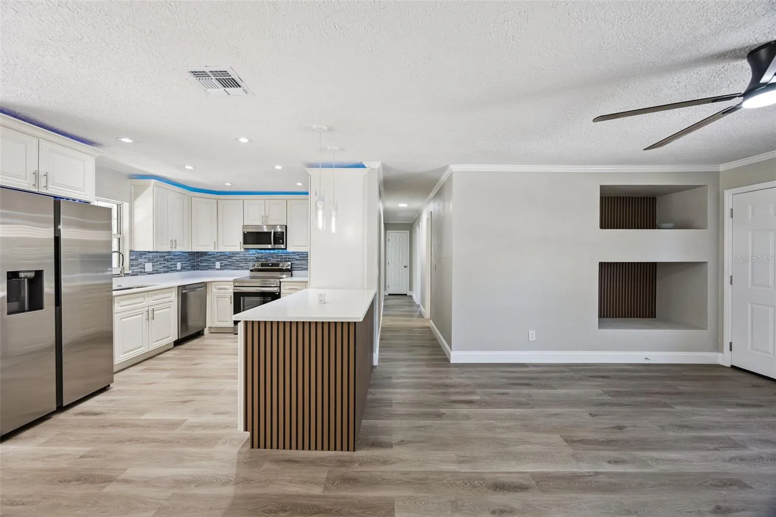 Open Living &amp; Kitchen Layout: Expansive view of the open living space and kitchen, highlighting luxury vinyl plank flooring, custom wood-slat island bar, and built-in wall display niches.