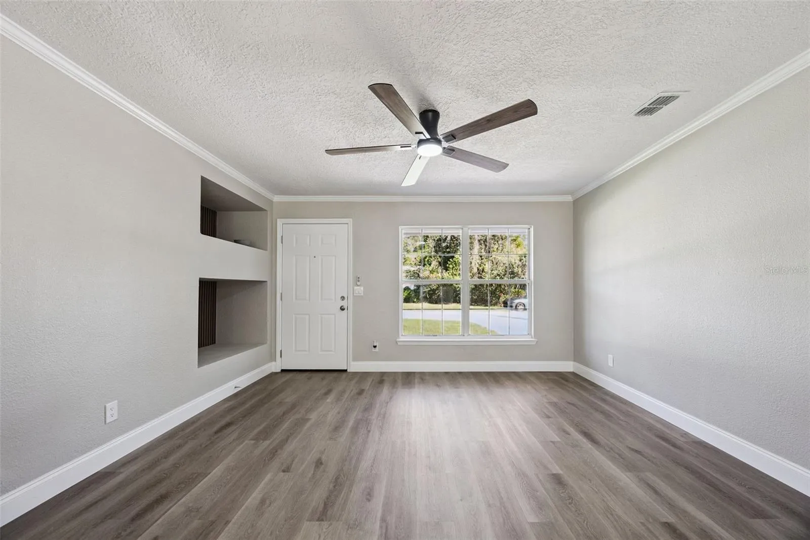 Front Living Space: Welcoming living area filled with natural light from large double windows, complete with smooth ceiling finishes, crown molding, and a modern fan