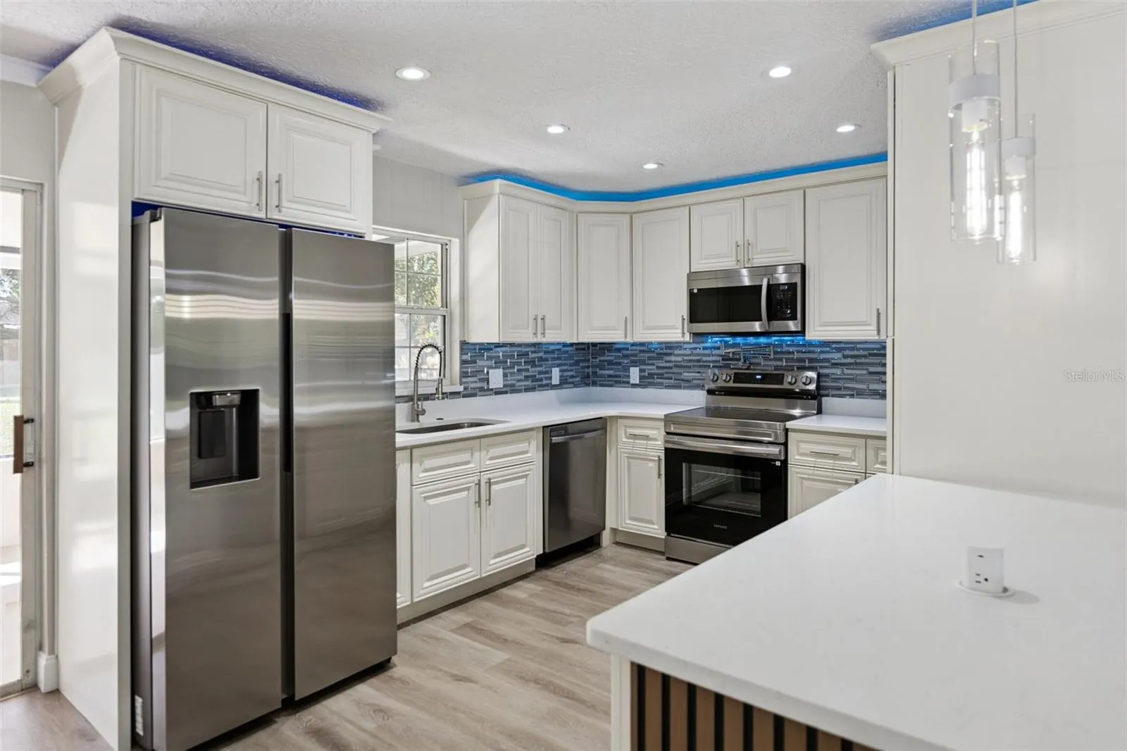 Gourmet Kitchen Corner: Upgraded kitchen perspective showcasing stainless steel appliances, raised-panel white cabinetry, quartz counters, and ambient ceiling lighting.