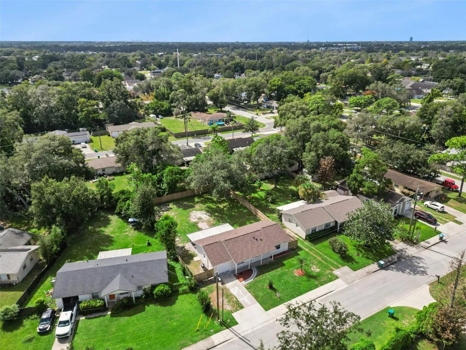 Aerial View of Property &amp; Street: Elevated perspective displaying the home's front elevation, driveway, screened porch, and lush lot along a quiet residential street.