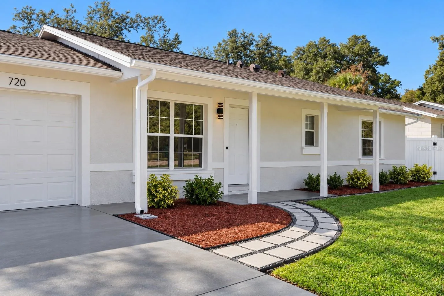 Garage &amp; Entry Perspective: Angled front view displaying the concrete driveway leading to the attached garage, decorative paver path, and covered entry porch.