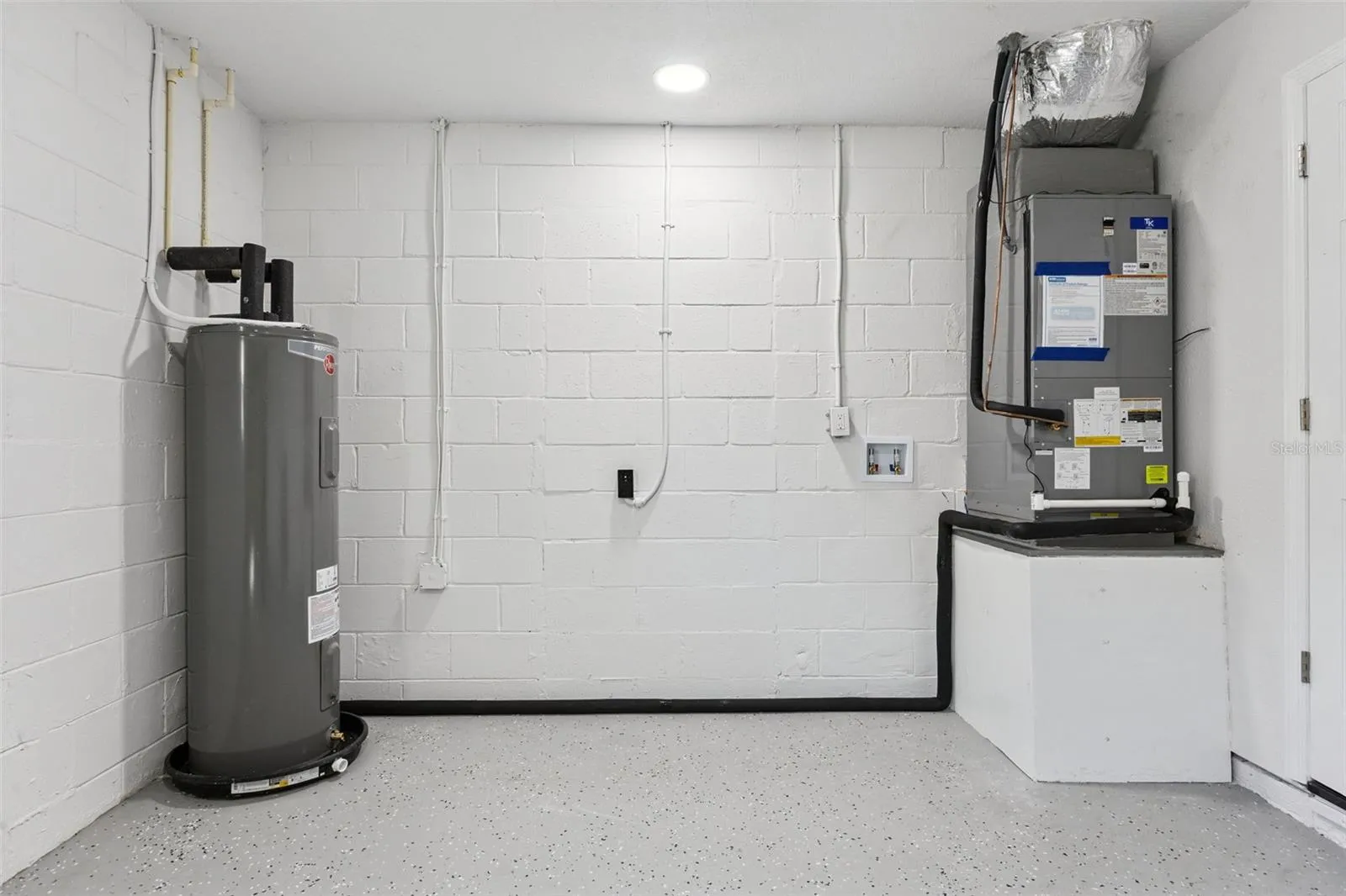 Garage &amp; Utility Space: Clean garage utility area featuring painted concrete block walls, durable speckled epoxy flooring, water heater, and HVAC equipment.