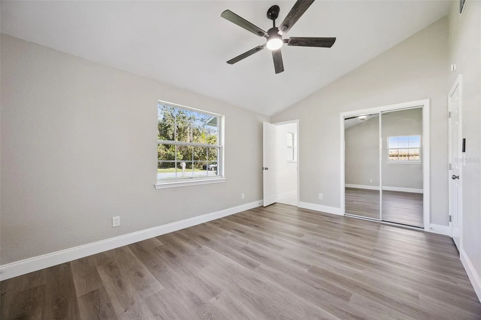 Primary Suite Alternate View: Generous primary bedroom layout highlighting high ceilings, neutral wall tones, bright window view, and built-in closet storage.
