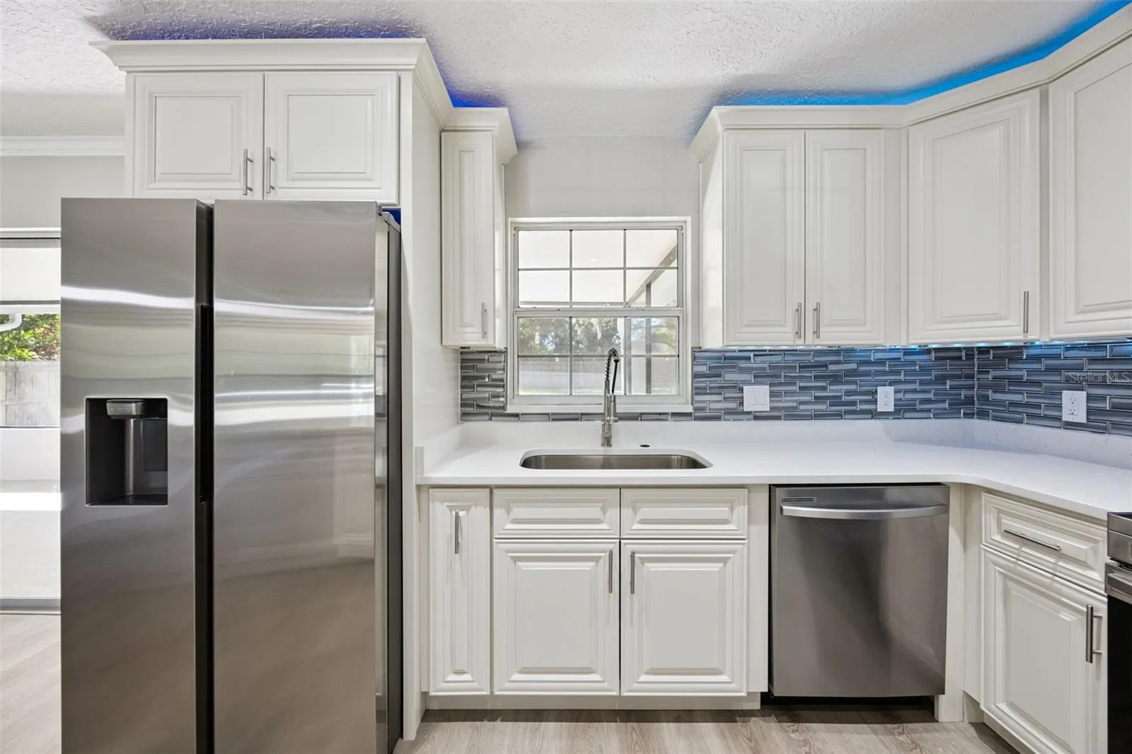 Kitchen Sink &amp; Appliance Suite: Kitchen workspace featuring an undermount sink under a bright window, gooseneck faucet, stainless dishwasher, French-door refrigerator, and mosaic backsplash.