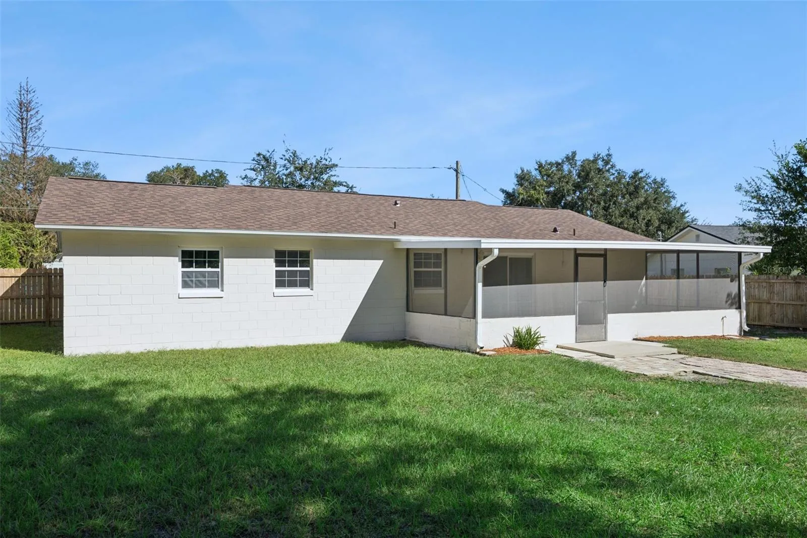 Full Rear Elevation: Single-story rear elevation featuring painted block construction, low-maintenance asphalt shingle roof, screened porch, and sprawling lawn.
