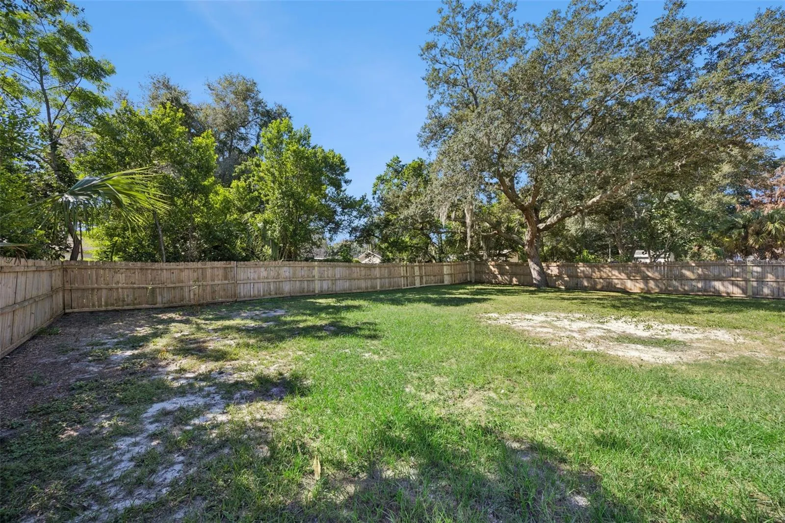 Fenced Perimeter: Clean view along the wooden privacy fence enclosure, showing the broad expanse of lawn and mature surrounding trees.