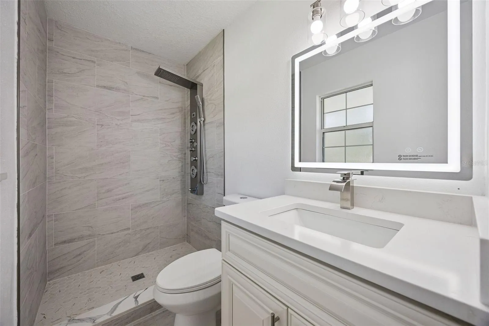 Primary Ensuite Bathroom: Modern primary bathroom complete with a white vanity, illuminated LED mirror, and tiled walk-in shower.