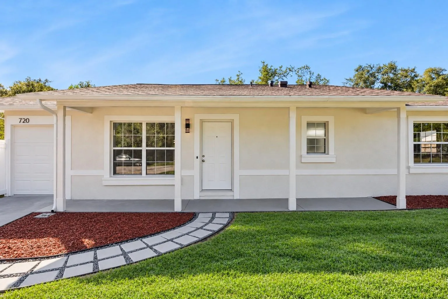 Covered Front Entry &amp; Walkway: Welcoming covered entryway featuring a custom paver walkway, fresh mulch landscaping beds, and a clean white front door