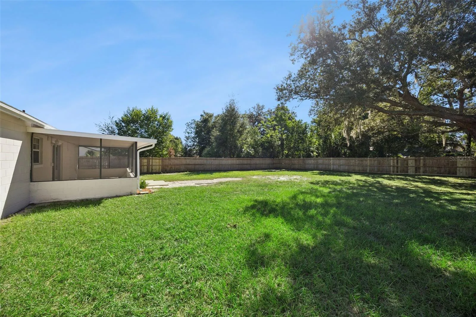 Rear Grounds &amp; Shade Tree: Corner view of the rear property showcasing the sprawling green lawn, screened patio, and mature trees.