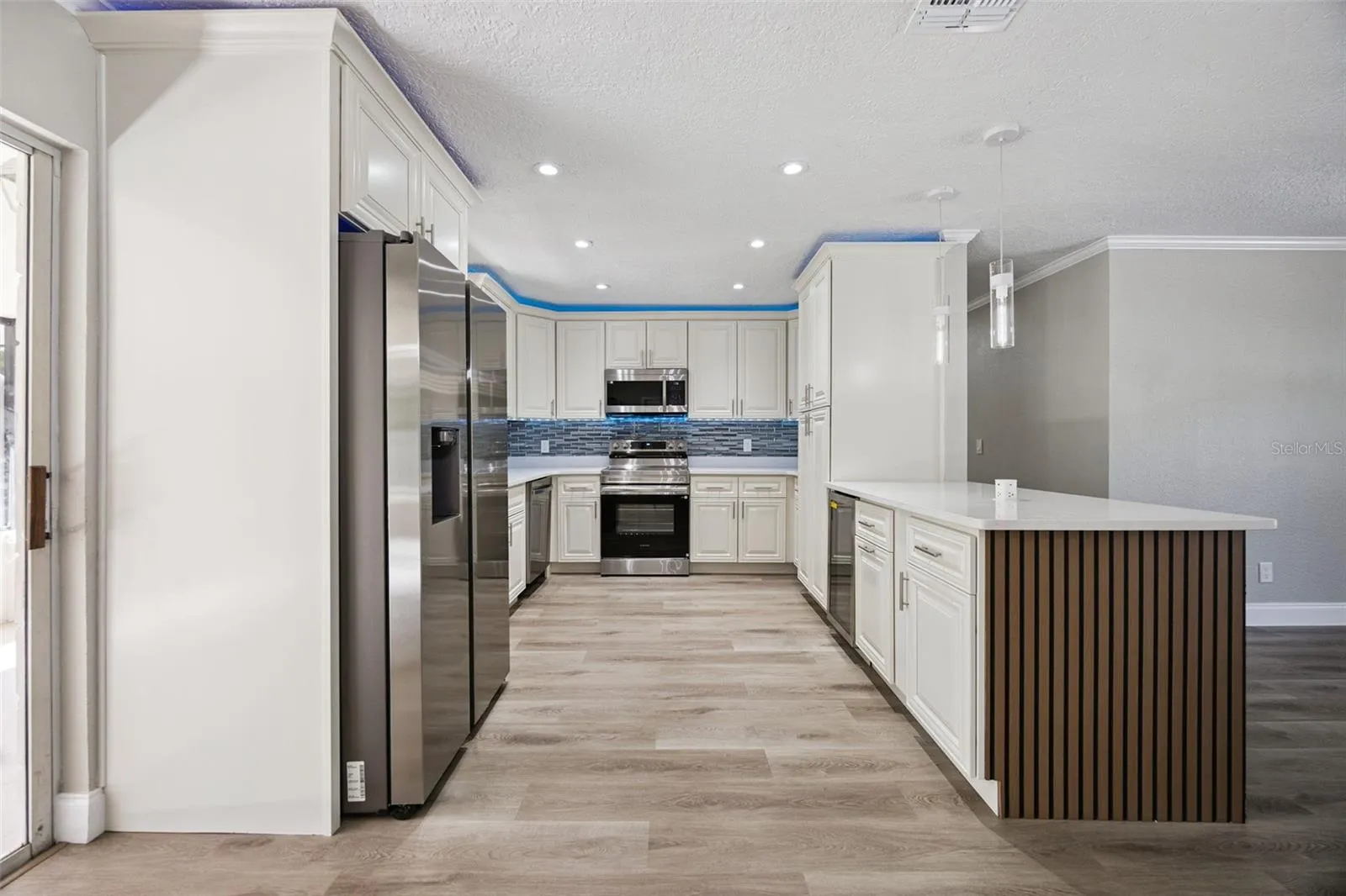 Refrigerator &amp; Kitchen Suite: Full kitchen perspective highlighting the stainless steel French-door refrigerator, quartz counters, slatted island peninsula, and adjacent sliding patio door.