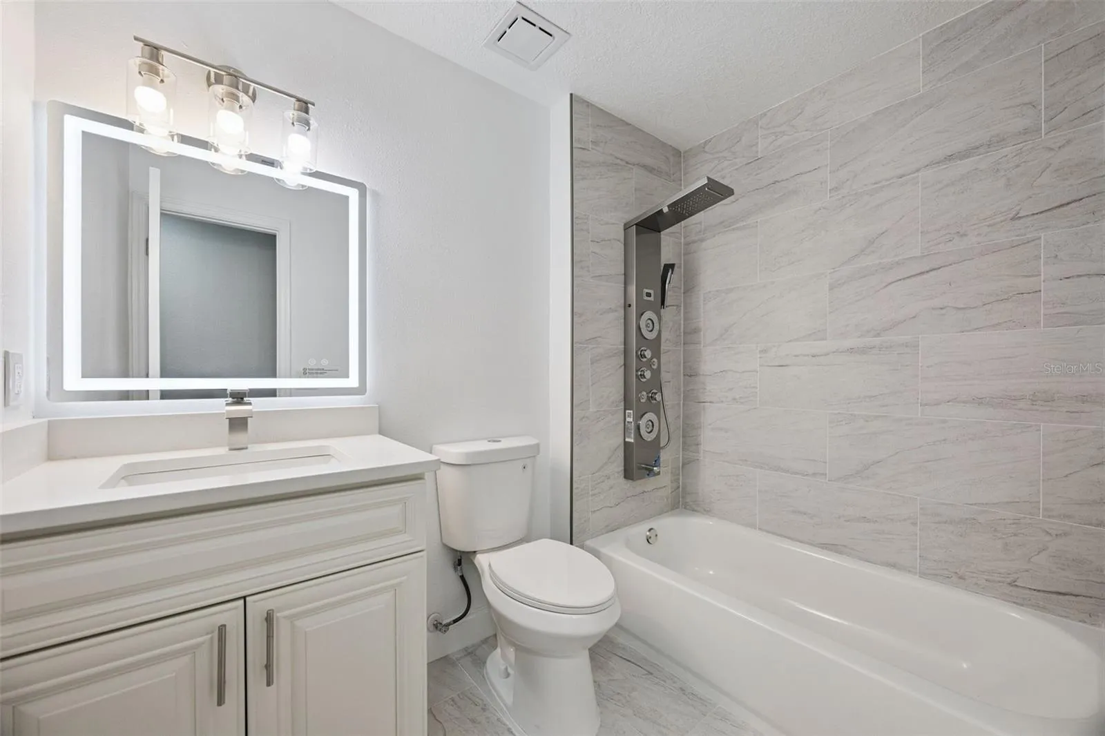 Full Guest Bathroom: Updated guest bathroom featuring a white quartz vanity, backlit LED mirror, tub/shower combination, and luxury shower tower