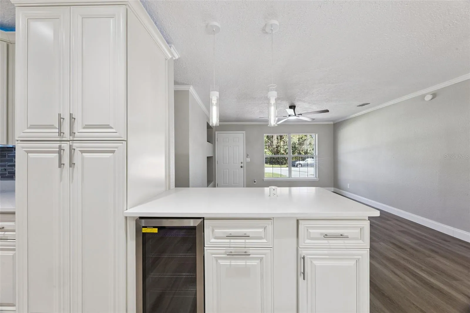 Island Peninsula &amp; Wine Cooler: Close-up view of the kitchen peninsula bar equipped with an under-counter wine fridge, quartz counter overhang, and sleek pendant lighting.