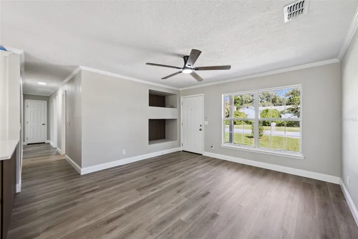 Living Room &amp; Recessed Niches: Spacious main living room highlighting built-in wall display niches, modern ceiling fan, large front window, and durable vinyl plank flooring