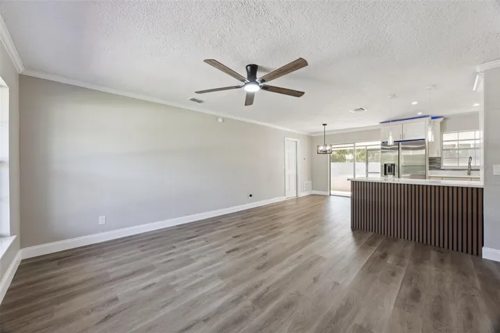 Living Room to Kitchen View: Expansive main living room highlighting fresh neutral tones, modern ceiling fan, and a custom wood-slat kitchen peninsula.