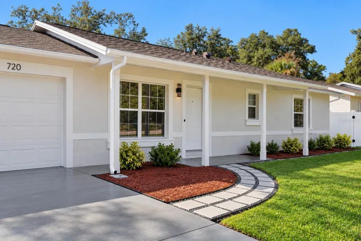 Garage &amp; Entry Perspective: Angled front view displaying the concrete driveway leading to the attached garage, decorative paver path, and covered entry porch.